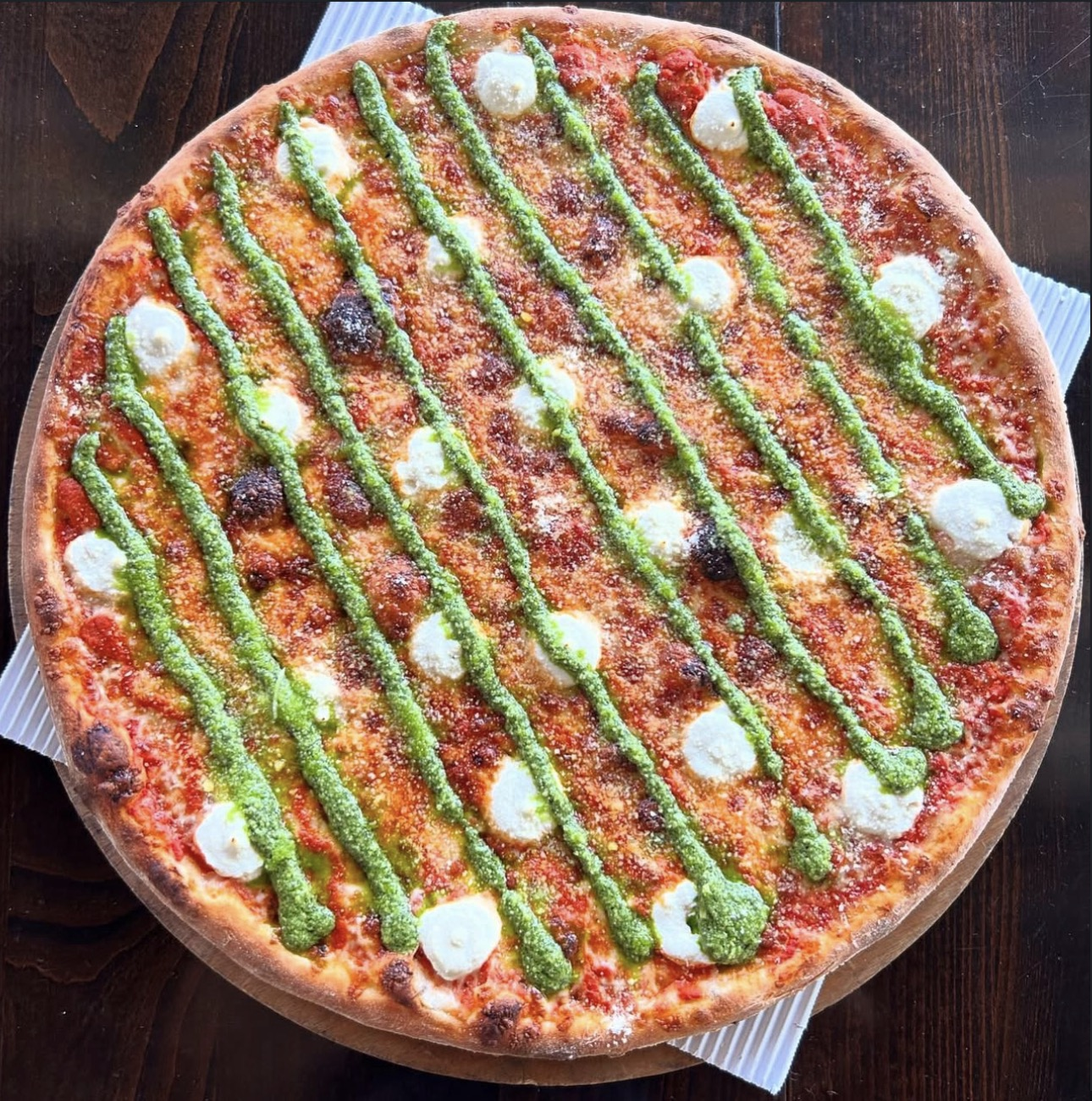 Pizza with ribbons of green pesto and dollops of white cheese.