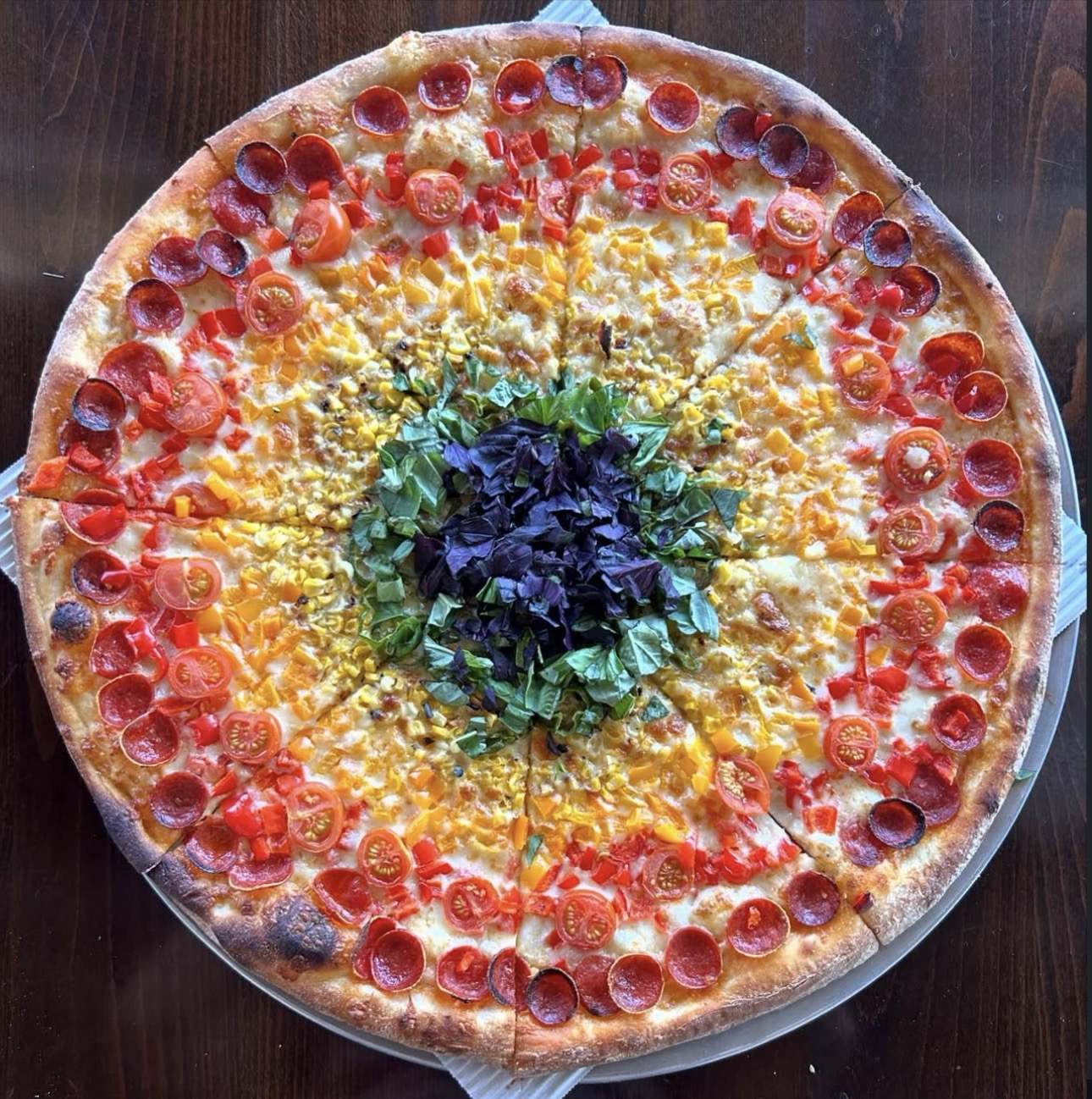 A colorful pizza with rings of vegetables, herbs, and pepperoni.